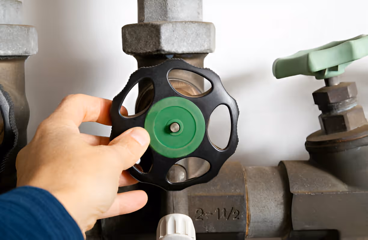 Hand turning green and black valve on industrial piping system