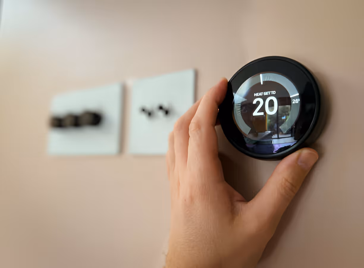 Hand adjusting smart thermostat displaying temperature of 20 degrees
