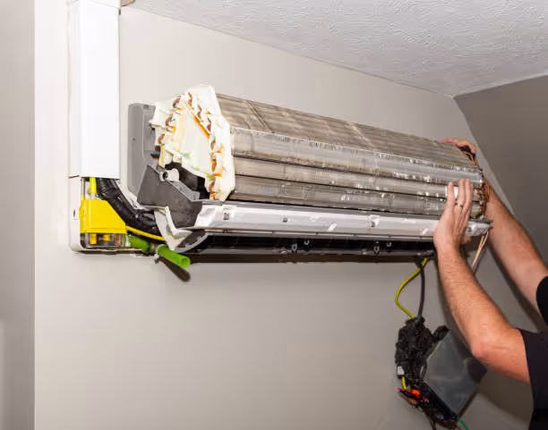 Technician cleaning and maintaining a wall-mounted air conditioning unit