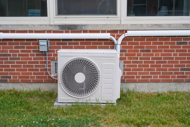 White air conditioning unit mounted on brick wall with electrical conduit