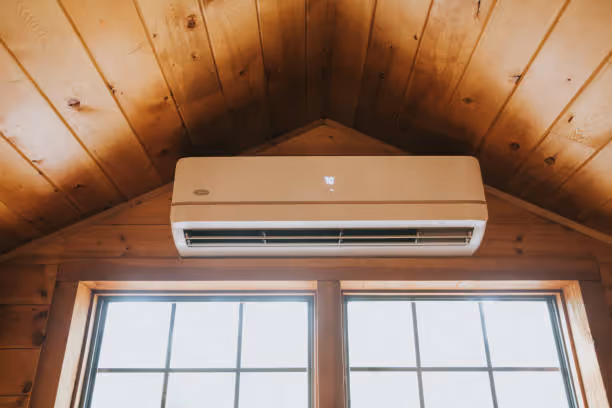 Wall-mounted air conditioner installed in a wooden cabin interior above a window