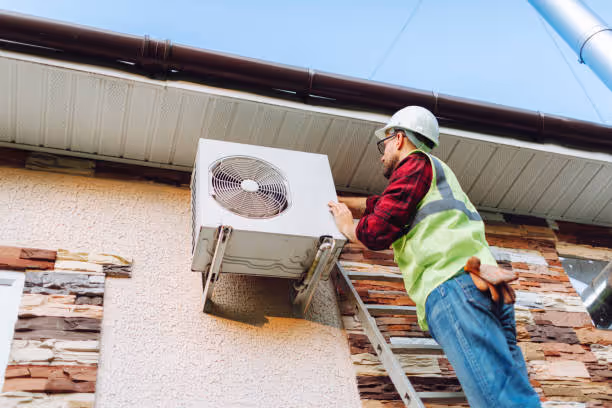 Worker in safety vest checks HVAC unit on ladder against building exterior