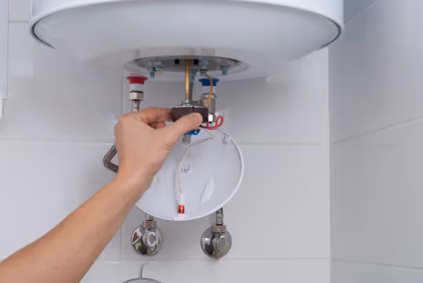 Hand adjusting temperature settings on a white electric water heater