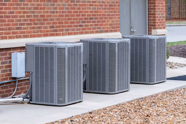 Multiple gray air conditioning units outside brick building on concrete pad