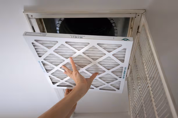 Hand removing clean air filter from ceiling vent or HVAC system