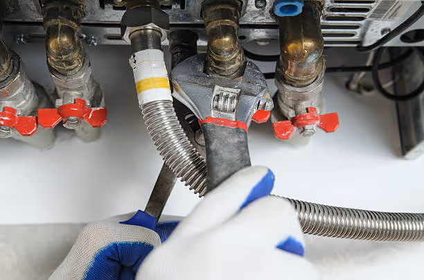 Gloved hand adjusting metal pipes with red valves on industrial equipment