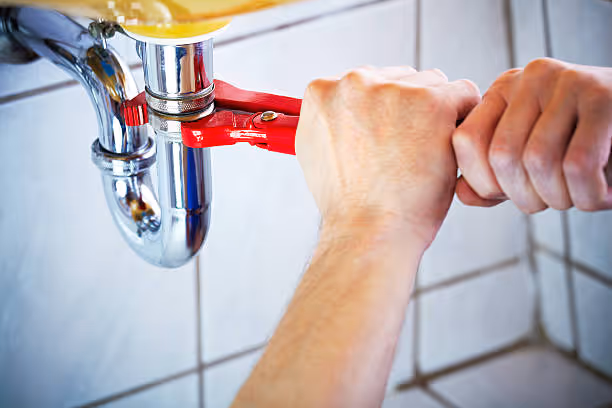 Hands using a wrench to tighten plumbing pipe under a sink