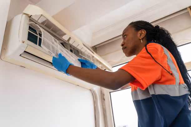 Technician in safety vest cleaning wall-mounted air conditioning unit
