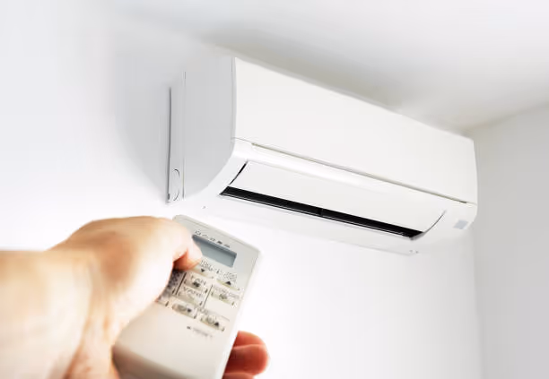 Hand holding remote control pointing at white wall-mounted air conditioner