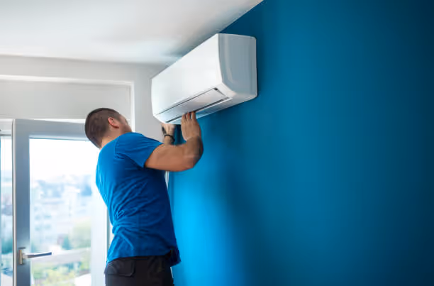 Technician installing wall-mounted air conditioning unit in blue room