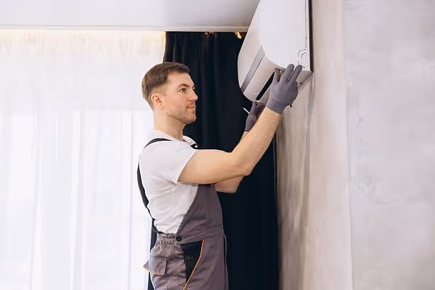 Worker in overalls smoothing wallpaper on white wall during renovation