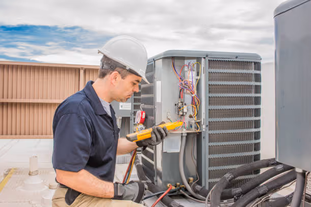 Technician in hard hat checking electrical connections on HVAC unit