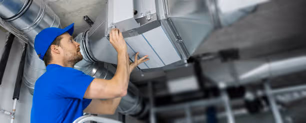 Technician in blue uniform inspecting industrial ventilation system