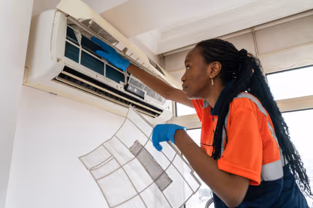 Technician in orange shirt cleaning and maintaining wall-mounted air conditioner