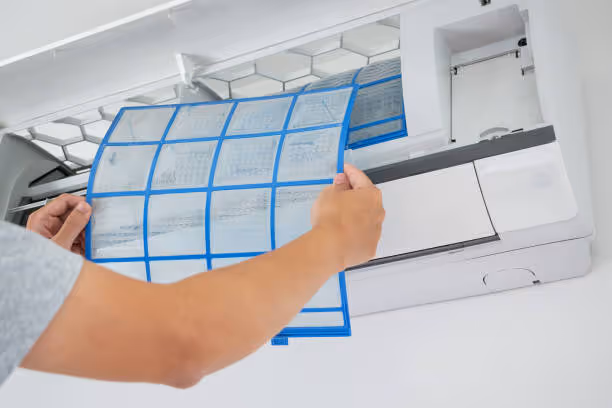 Person removing blue-lined air filter from white air conditioning unit