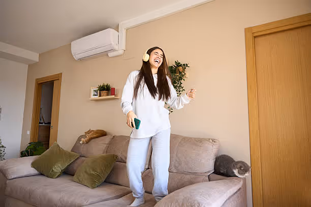 Woman in white loungewear jumping joyfully on cozy living room couch