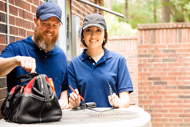Two workers in blue uniforms and caps standing by brick wall