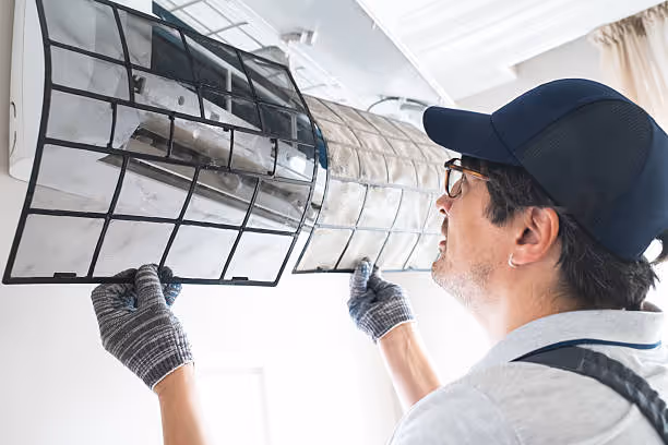 Technician in cap and gloves installing or repairing wall-mounted air conditioning unit