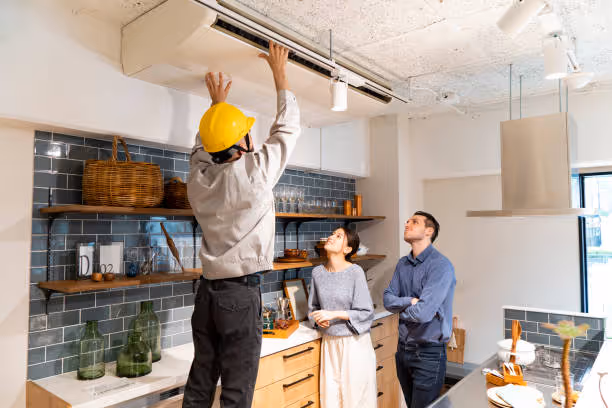 Worker in yellow hard hat installing air conditioning unit in kitchen
