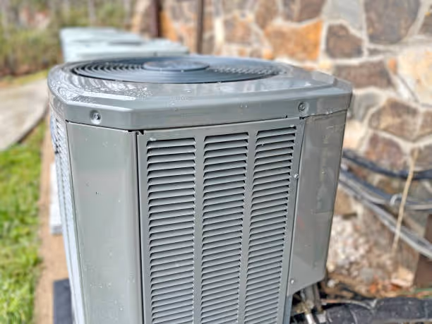 Gray outdoor air conditioning unit next to stone wall and grass