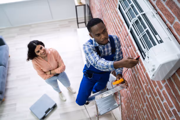 Technician installing air conditioner unit on brick wall with person watching