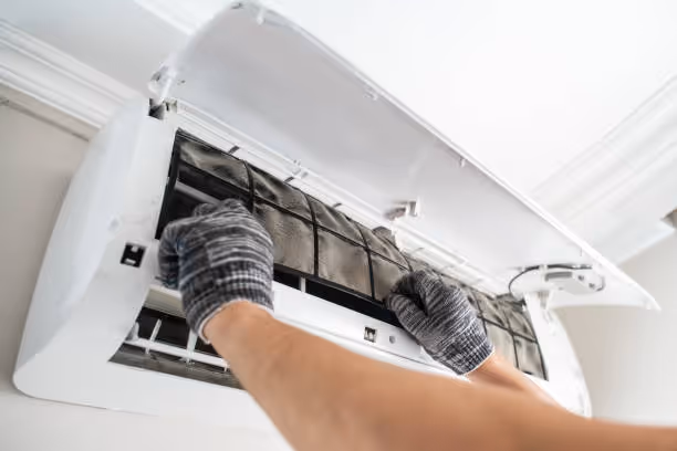 Hands in gloves cleaning air conditioning filter inside wall unit