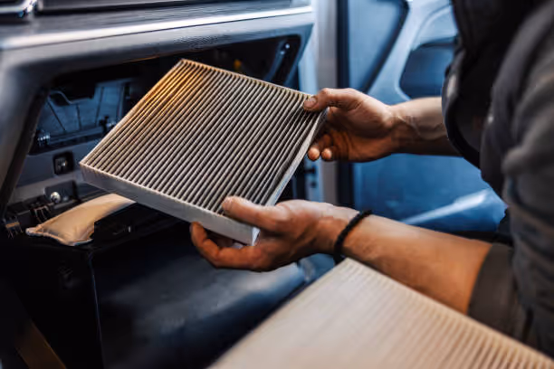 Hands removing a car cabin air filter from vehicle dashboard