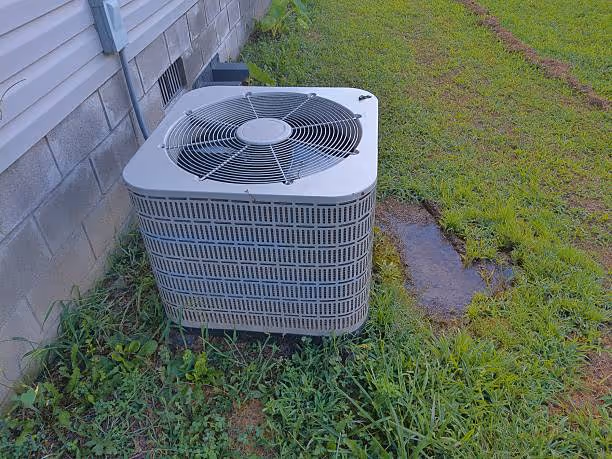 Outdoor air conditioning unit sitting on grass next to a house foundation