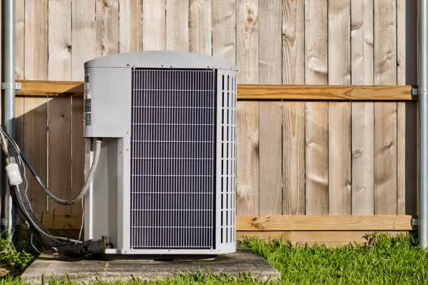 Air source heat pump unit installed next to wooden fence and grass