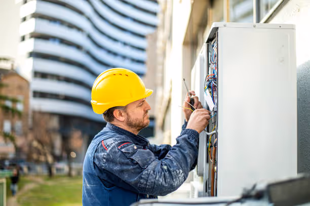Technician in yellow hard hat repairing electrical panel outdoors