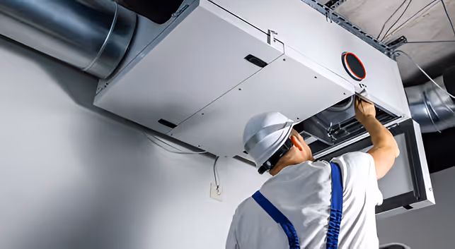Technician in hard hat inspecting industrial HVAC system ceiling unit