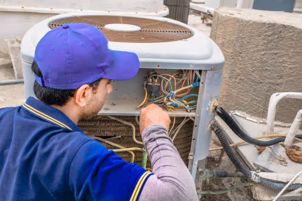Technician in blue cap repairing electrical wiring in outdoor HVAC unit