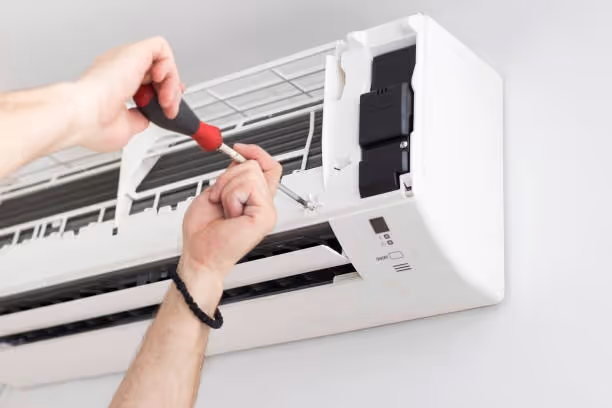 Technician repairing air conditioning unit with screwdriver