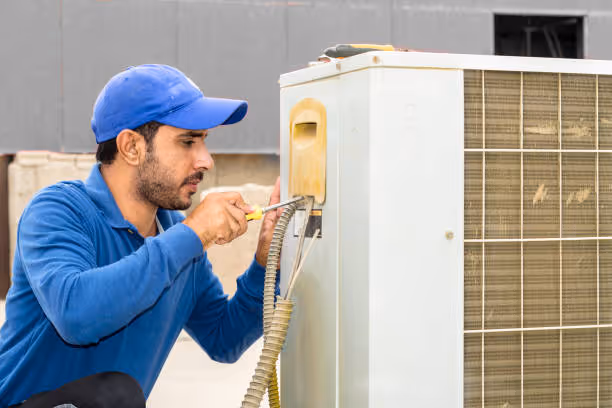 Technician in blue cap repairing air conditioning unit with tools
