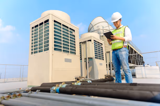 Technician in safety vest checks HVAC units on rooftop with clipboard