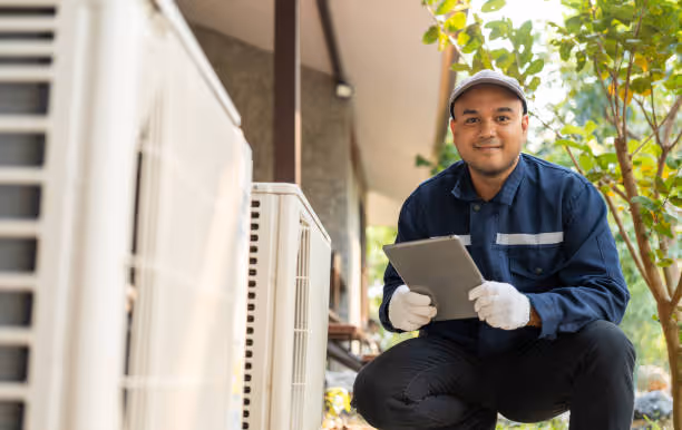 Technician in blue uniform checking HVAC unit with tablet outdoors