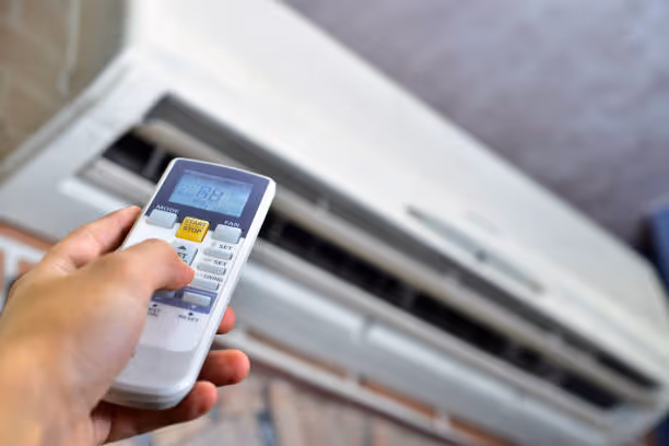 Hand holding remote control adjusting air conditioning unit