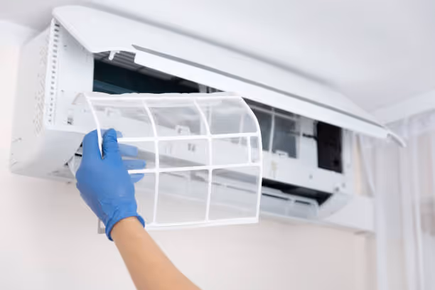 Hand in blue glove removing air conditioner filter for cleaning