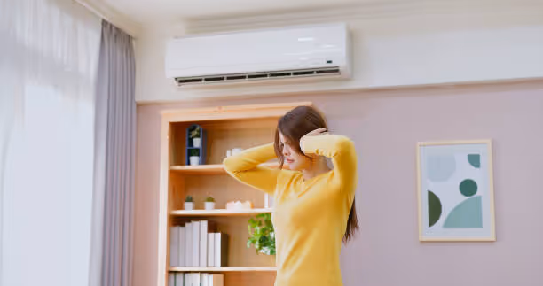 Woman in yellow sweater adjusting air conditioner in bright home interior