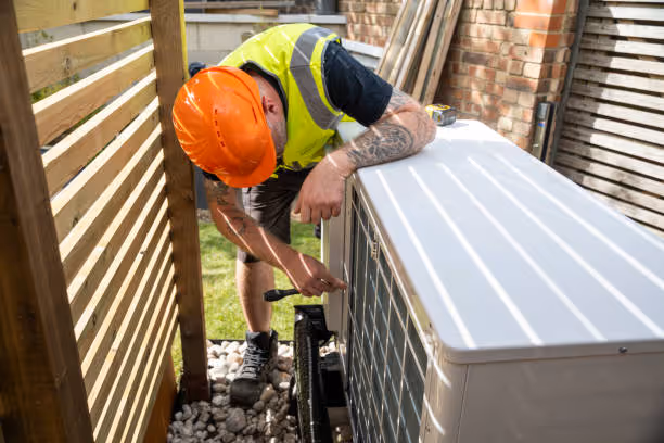 Construction worker in safety gear installing equipment next to brick wall