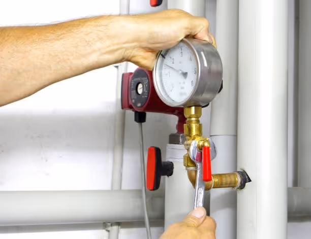 Hand adjusting pressure gauge on industrial piping system