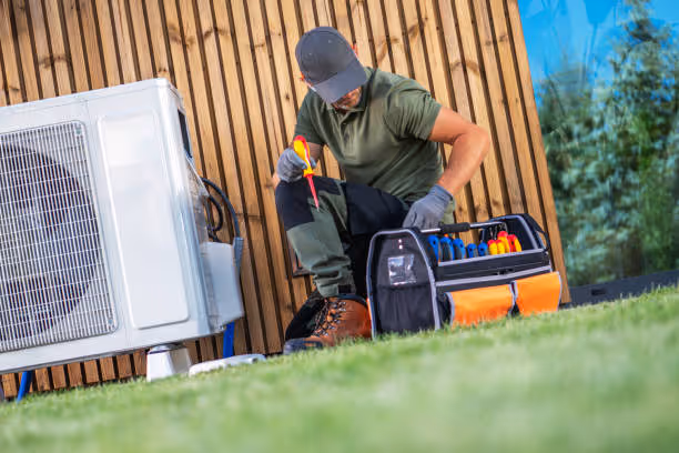 HVAC technician working on outdoor air conditioning unit with tools