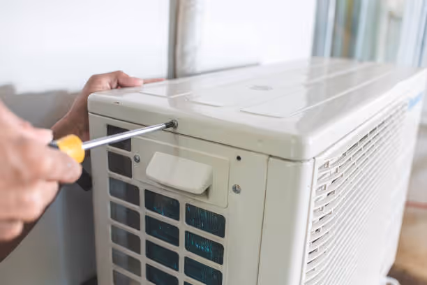 Technician repairing air conditioning unit with screwdriver