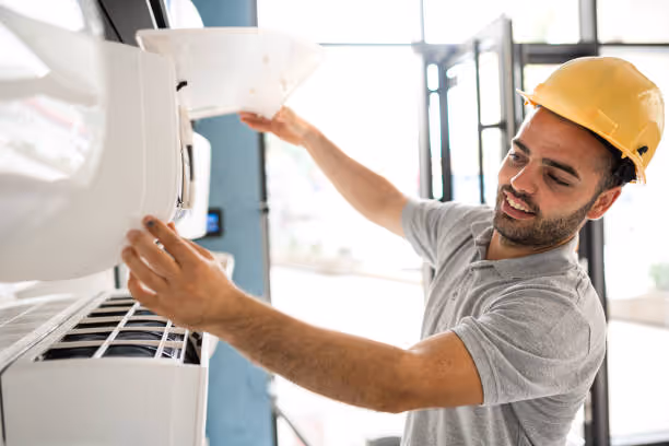 Worker in yellow hard hat installing or repairing air conditioning unit