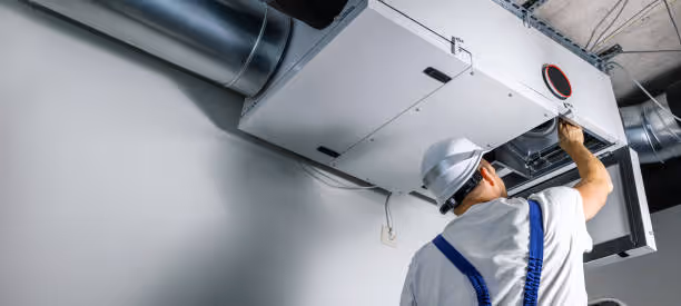 Technician in hard hat inspecting industrial ventilation system ductwork