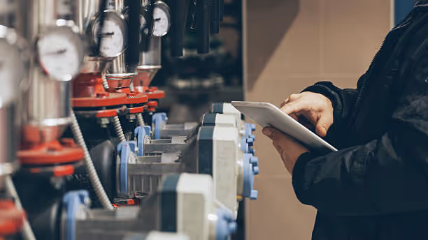 Technician checking industrial machinery with tablet in manufacturing facility
