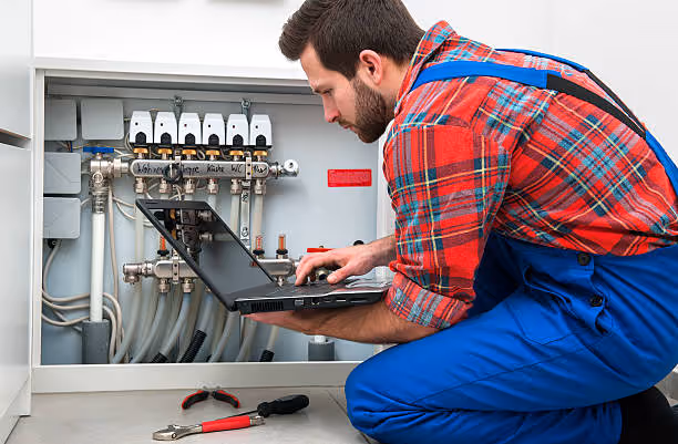Technician in plaid shirt checking heating system with laptop