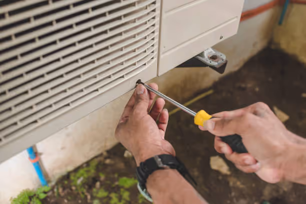Hands using screwdriver to repair or install an air conditioning unit