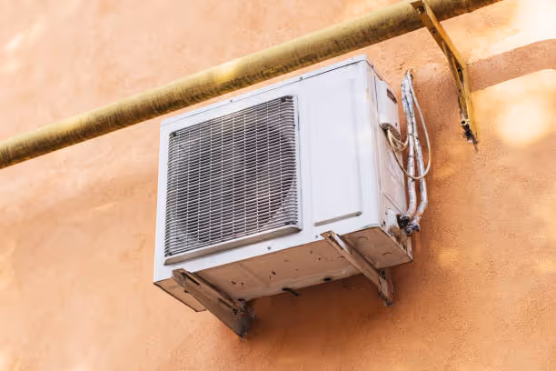 White air conditioning unit mounted on peach-colored wall with golden pipe