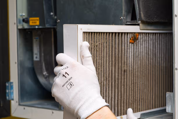 Gloved hand checking a dirty air filter near an HVAC system